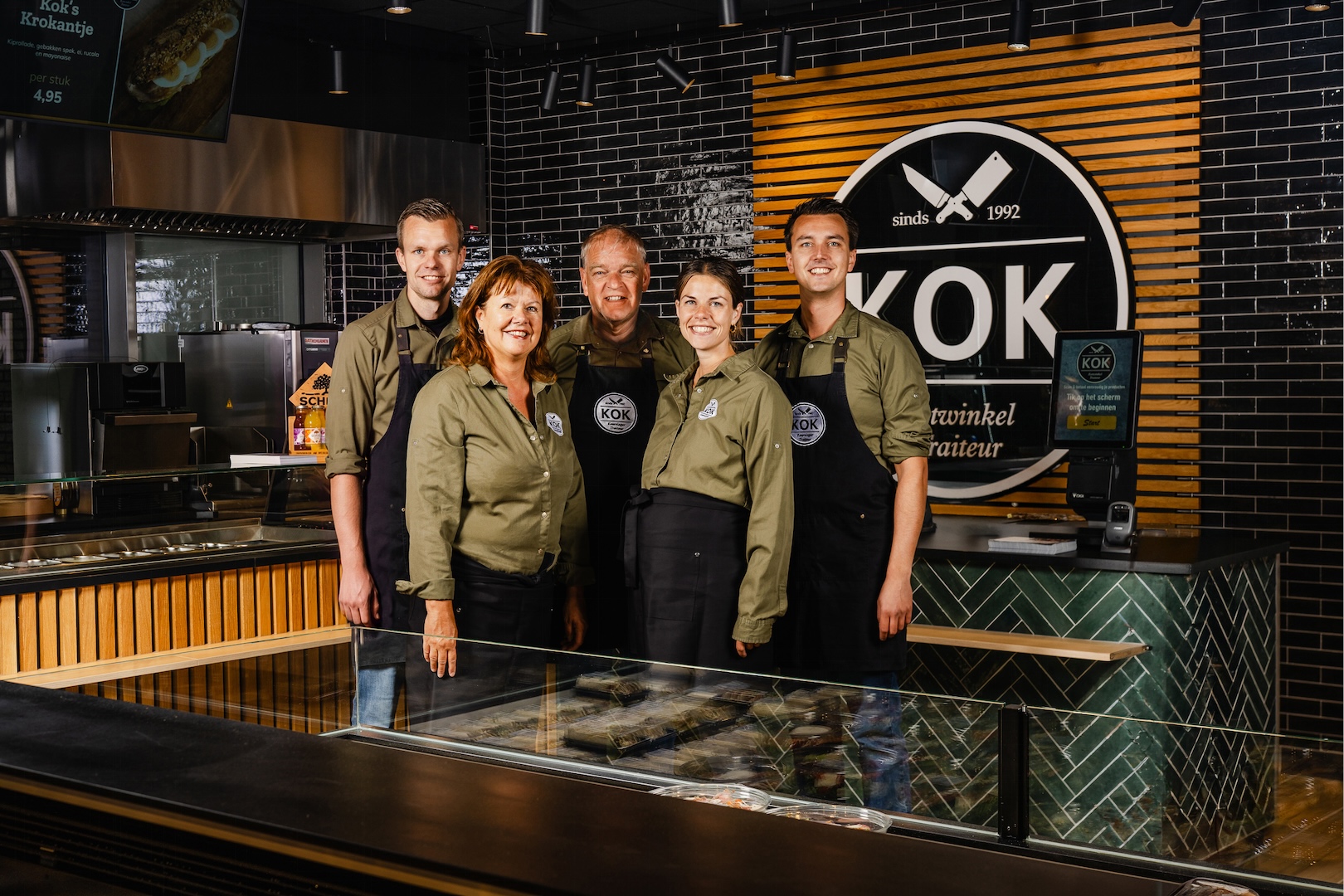 Het team van Keurslager en traiteur Kok voor de toonbank, met het eigen KOK-logo op de achtergrond